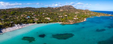 İtalya 'da bir Sardunya sahilinin havadan görünüşü, turkuvaz suları, güneş banyosu yapan kumlu kıyı şeridi, sahil şemsiyeleri ve kıyı boyunca yemyeşil.