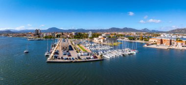 Olbia, Sardinya 'nın havadan görünüşü, yatları, dönme dolabı ve berrak mavi gökyüzü ve sakin suların altındaki dağları gösteren bir marina..