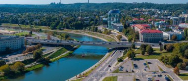 Vilnius, Litvanya 'nın hava perspektifi, Neris Nehri' ni gösteriyor, araçları olan bir köprü, bir tekne, modern ve tarihi binalar, ve yemyeşil alanlar.