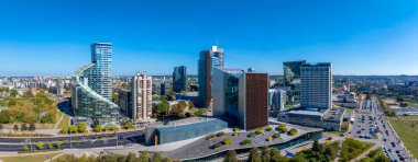 Yüksek binalar, yeşil alanlar ve açık mavi gökyüzü altında hareketli yollar arasında Europa Kuleleri 'nin spiral tasarımının yer aldığı Vilnius, Litvanya manzarası.