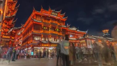 Geleneksel Çin binaları Yu Garden, Şangay 'da gece gökyüzüne karşı sıcak bir şekilde parlarken, kalabalıklar sahneye dinamik bir atmosfer ekliyor..