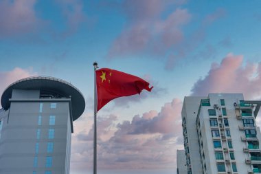 A Chinese flag waves prominently with a pink and blue sky backdrop. A modern building with a circular rooftop and a high rise residential building are visible. clipart