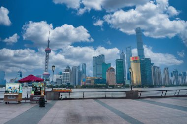 Bund, Oriental Pearl Tower, Shanghai Tower ve Jin Mao Tower ile Şangay 'ın ufuk çizgisi. Tedarikçi tezgahlarıyla dolu bir nehir kenarı gezinti alanı ön planda..