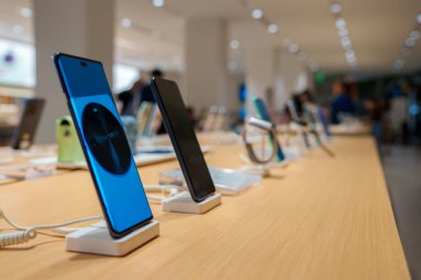 Şangay 'daki iyi aydınlatılmış bir elektronik mağazasında ahşap bir masanın üzerinde bir sıra akıllı telefon bulunuyor. Gösterişli, minimalist tasarım yüksek teknoloji ürünlerini ön plana çıkarıyor..