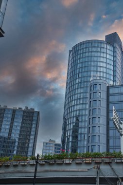 Görüntü, Şangay 'ın modern gökdelenini akşam gökyüzünü yansıtan silindirik cam bir gökdelenle, yüksek binalarla çevrili bir çatı bahçesi ile yakalıyor..