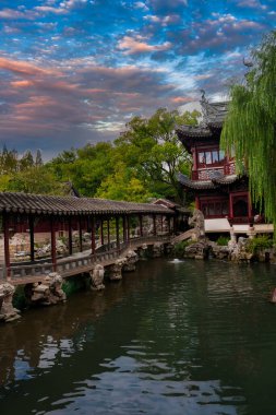 Geleneksel bir Çin pavyonu, Şangay 'daki Yuyuan Garden' da yemyeşil ve renkli bir gökyüzünün altında kemerli bir köprüyle çevrili sakin bir göletin yanında duruyor..