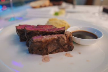 Bir tabakta, içinde pembe bir iç ve kurumuş bir sos bulunan orta pişmiş biftek dilimleri sergileniyor. Arkaplan hafifçe bulanık.