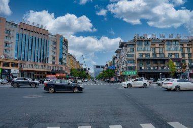 Şangay, Çin 'de yoğun bir kavşak, bulutlu mavi bir gökyüzünün altında. Sokakları arabalar ve yayalarla dolduran modern ve geleneksel tarzda binaların ortası..