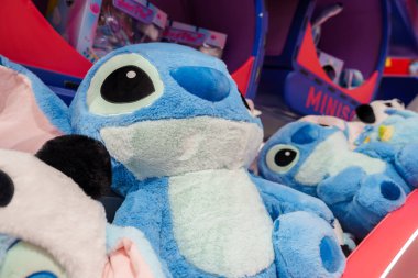 Geniş gözlü ve küçük burunlu mavi pelüş oyuncak koleksiyonu, canlı pembe ve mavi renk şeması içeren bir mini markette raflarda sergileniyor..