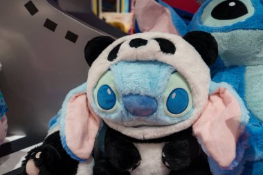 Disney 's Lilo and Stitch' ten lüks bir Stitch oyuncağı büyük mavi gözleri ve pembe kulakları olan bir panda kostümü giyer. Arka planda başka bir oyuncak görünüyor.