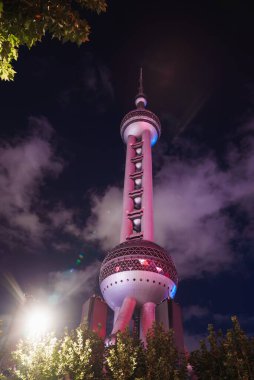 Doğu İnci Kulesi Çin 'in Şangay şehrinde gece gökyüzüne karşı ışıldıyor. Işıklar küresel dizaynını ve tabanındaki ağaçları aydınlatıyor..