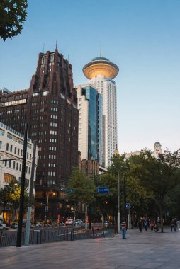 Radisson Blu Hotel 'in UFO' sunu gösteren hareketli Şangay sokak sahnesi. Restoran ve Art deco Park Oteli gibi, açık gökyüzü altında ağaçlar ve yayalar var..