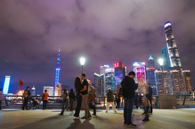 Shanghai 'nin Pudong bölgesi geceleri gökyüzüne yükseliyor, aydınlık Doğu İnci Kulesi ve Şangay Kulesi yer alıyor. İnsanlar Bund rıhtımında toplanıyor..