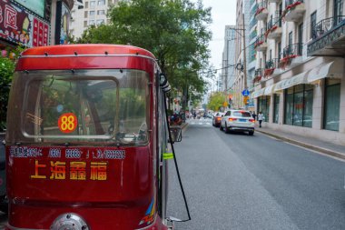 Çince karakterli kırmızı motorlu bir triportör ve 88 numara modern binalar ve yeşilliklerle dolu kalabalık bir Şangay caddesinde göze çarpıyor..