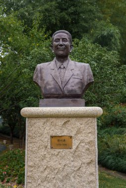 Takım elbiseli ve kravatlı bir adamın 1918 1999 tarihli taş bir heykel üzerindeki bronz büstü Şangay parkında ağaçlar ve çalılarla çevrili..