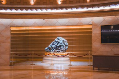 Kapalı alanda kırmızı bir halat bariyeriyle çevrili ayrıntılı bir heykel sergilenmektedir. Sıcak, altın rengi duvar ve eşsiz tavan ışıkları atmosferi güçlendirir..