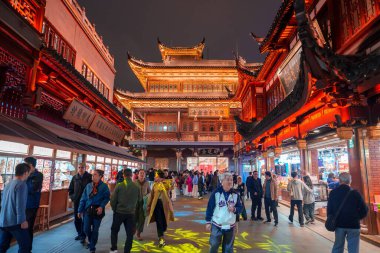 Geleneksel Çin mimarisi süslü çatıları ve ahşap oymaları geceleri aydınlatılır. İnsanlar hareketli, ışıl ışıl caddelerde alışveriş yaparlar..