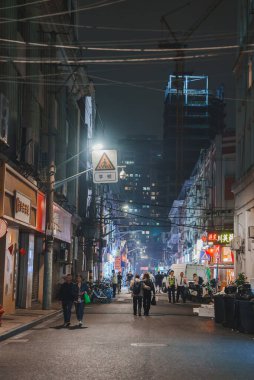 A vibrant Shanghai street at night features neon lit shops and eateries. Pedestrians walk along the bustling street, with a crane and construction site visible. clipart