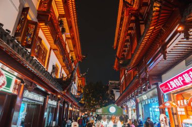 Shanghais 'in eski kasabasında süslü saçakları ve neon tabelaları olan geleneksel Çin mimarisi. Kalabalık caddede dükkanlar ve gıda tezgahları.