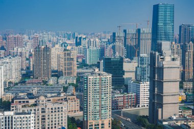 Görüntüde Şanghay kentsel manzarası görülüyor, modern gökdelenler, eski binalar ve turnalar açık mavi gökyüzü altında, hızlı gelişmeyi gösteriyor..