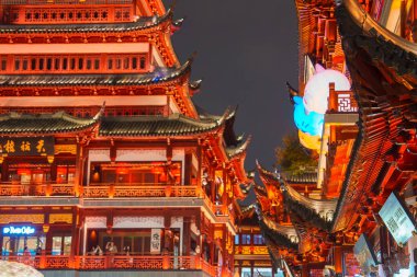 Şangay 'daki geleneksel Çin binaları geceleri sıcak ışıklarla parıldıyor. Neon işaretleri ve büyük bir fener tarihsel ortama modern elementler ekler..