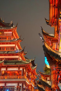 Intricately designed pagoda style buildings in Shanghai's old town are illuminated by warm lights, showcasing ornate details and curved roofs against a night sky. clipart