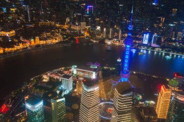 The image depicts Shanghai at night, featuring the illuminated Oriental Pearl Tower in blue. The Huangpu River separates Pudong's skyscrapers from the Bund's historic buildings. clipart