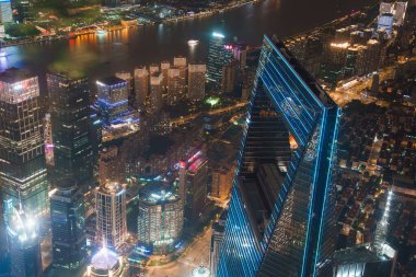 The Shanghai World Financial Center stands illuminated with blue edges, surrounded by vibrant skyscrapers and the Huangpu River under the night sky. clipart