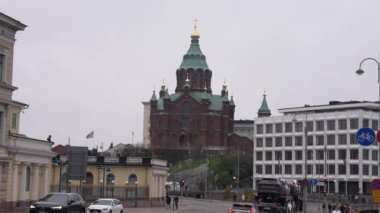 Uspenski Katedrali 'nin kırmızı tuğla cephesi ve Helsinki' nin bulutlu gökyüzü altındaki tarihi ve modern binaların karışımı ortasındaki yeşil kubbelerin manzarası.