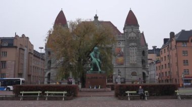 Fin Ulusal Tiyatrosu ve Aleksis Kivi heykelinin yer aldığı Helsinki şehir merkezinin sonbahar yeşillikleri ve kentsel yaşamla çevrili görüntüsü.