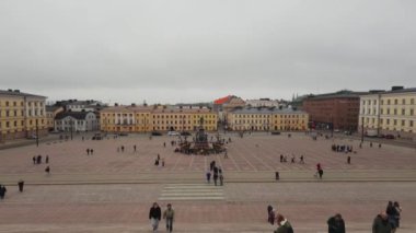 Helsinki Senato Meydanı manzarası, neoklasik binalar ve II. Alexander heykeli yer alıyor. Kış kıyafetli yayalar serin bir gün öneriyor.