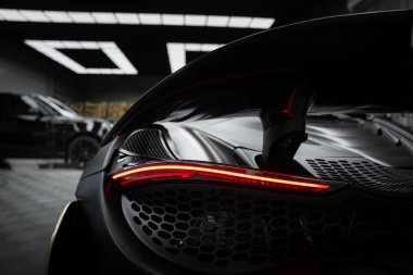 Görüntü McLaren 720 S 'nin arkasını yakalar, aerodinamik tasarımını, karbon fiber detaylarını ve modern kapalı sergi salonunda kendine özgü arka ışığını gösterir..