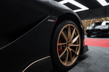Bir McLaren 720S parlak tasarımı ve bronz alaşımlı tekerlekleriyle sergilenir. 720 S rozeti görünür, arka planda Lamborghini Urus Performante var..
