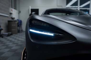 Görüntü, kendine özgü LED şeritli bir McLaren 720S far tasarımı yakalıyor. Mat siyah kaplama kareli zemine ayarlı.