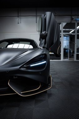 McLaren 720S, altın kaplamalı bir mat siyah kaplama ile kapalı alanda sergilenmektedir. Açık kelebek kapısı ve endüstriyel ayarı vurgulandı.