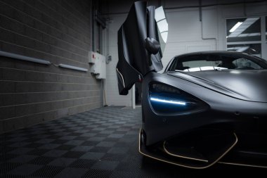 McLaren 720S, aerodinamik tasarımı ve LED farlarıyla kapalı bir katta sergilenmektedir. Tuğla duvar ve boru görünür..