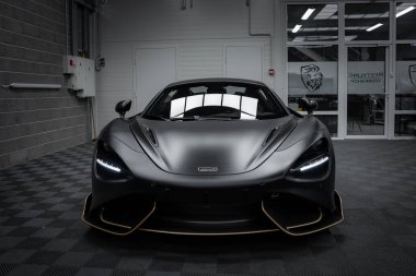 Mat siyah kaplamalı ve altın aksanlı bir McLaren 720S süper araba modern bir otomotiv atölyesinde kapalı bir zemine park edilmiştir..