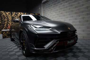 Bir mat siyah Lamborghini Urus Performante kapalı bir yerde, arka planda karmaşık altın desenli dekoratif bir duvarla sergilenir..