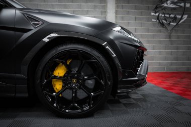 Görüntü Lamborghini Urus Performansının siyah alaşımlı jantları ve sarı fren ayarlarıyla gri tuğla duvara dayalı ön tekerleğini gösteriyor..