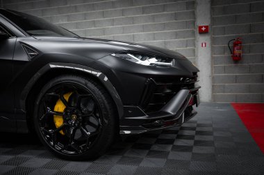 Lamborghini Urus Performante 'nin ön bölümü mat siyah kaplama, siyah jantlar ve gri tuğla duvarlı bir galeride sarı fren ayarları..
