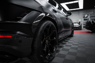 Lamborghini Urus Performante 'nin bir sergi salonunda mat siyah kaplama görüntüsü. Damalı zemin ve parlak ışıklandırma tasarımını vurgular.