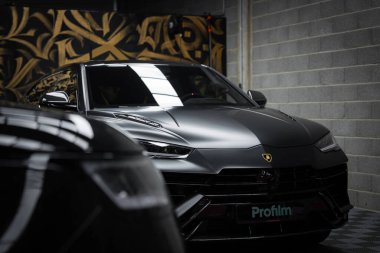 Lamborghini Urus Performante siyah kaplamalı loş bir garajda sergileniyor. Arkaplanda altın ve siyah soyut desenler yer alıyor.