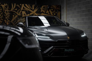 Lamborghini Urus Performante 'nin yakın plan görüntüsü, siyah kaplamalı, altın ve siyah desenli bir duvara karşı, lüks bir galeride..