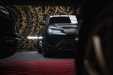 Lamborghini Urus Performante 'nin yakın plan görüntüsü, arka planda altın ve siyah desenler. Kırmızı ve siyah kareli döşeme görünür.