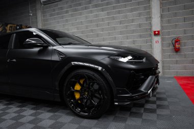 Görüntü siyah Lamborghini Urus Performansını içeriyor, keskin çizgilerle ön kısmına odaklanıyor, kapalı bir zemine park etmiş..