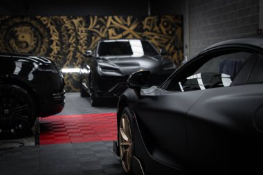Siyah renkli Lamborghini Urus ve kırmızı ve siyah kareli zeminde altın tekerlekleri olan altın desenli bir McLaren 720S..
