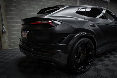 Görüntü Lamborghini Urus Performante 'yi içeriyor. Kapalı bir zemine park edilmiş, mat siyah kaplamalı. Arka vitrinler arka farlar ve arka avlu egzozları.