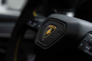 Görüntü, Urus Performante direksiyonundaki Lamborghini amblemini yakalıyor. İçi lüks detaylarla dolu siyah bir arka planda altın bir boğa var..