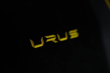 The image shows a close up of the word 'URUS' in bright yellow embroidery on a dark fabric, highlighting the luxury detailing of a Lamborghini Urus Performante. clipart