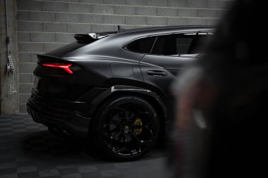 Görüntü, Lamborghini Urus Performansını siyah kaplamayla yakalıyor ve arka tarafına odaklanıyor. Döşeme döşeme ve beton duvarlar kapalı alanda görülebilir..